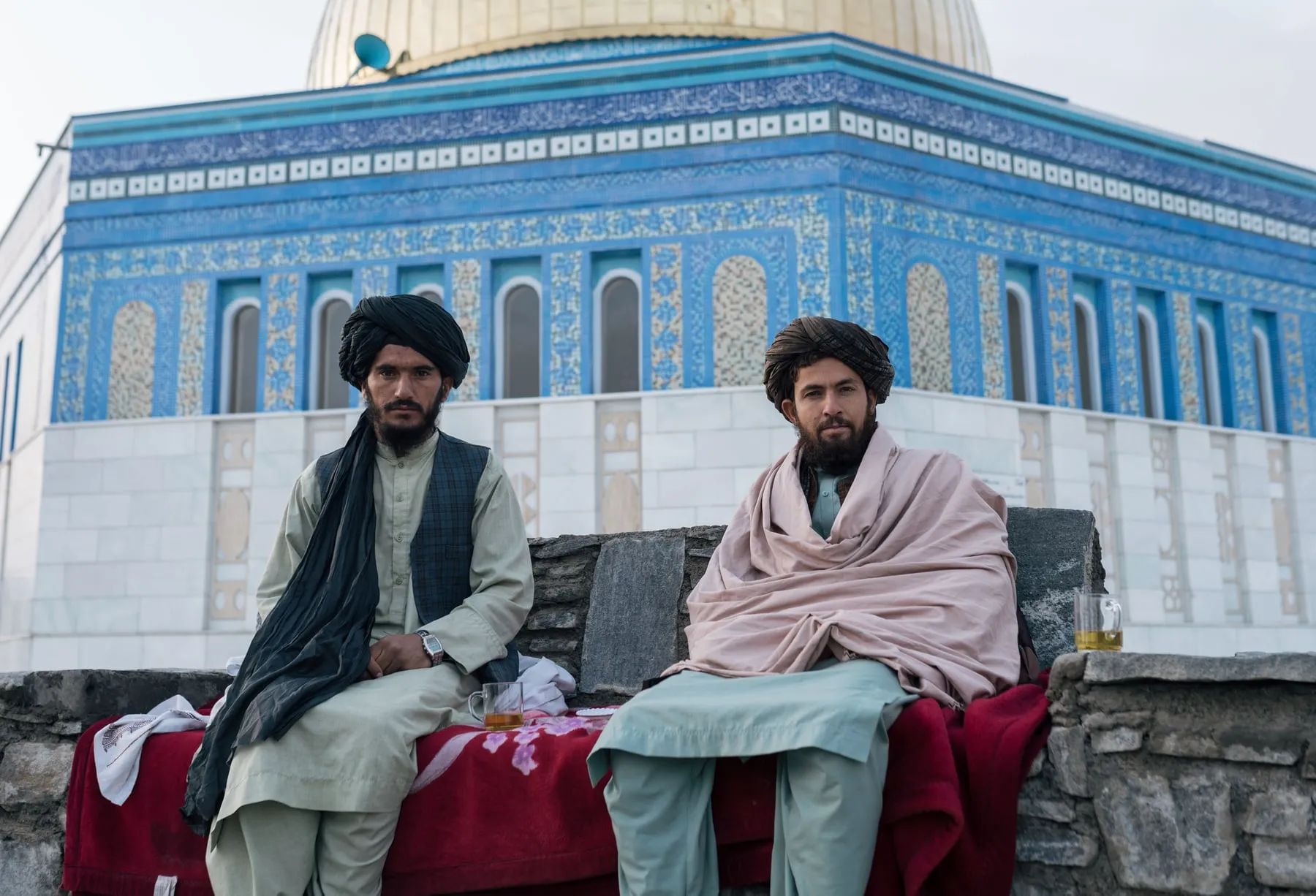 Zwei Männer sitzen bei Tee vor einer blau gekachelten Moschee in Afghanistan